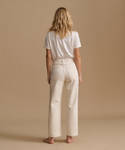 A model wearing a white t-shirt with cream color jeans in a studio.