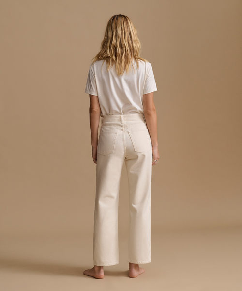 A model wearing a white t-shirt with cream color jeans in a studio.