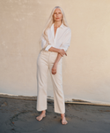 A model wearing a white button up shirt with cream color jeans at the beach.