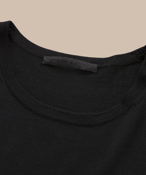 Close-up of the neckline of the Merino Tank in black, featuring a visible jenni kayne label against a beige background—perfect as a stylish base layer.