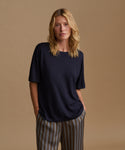 A model wearing a navy blue tee with stripe pants against a beige background.