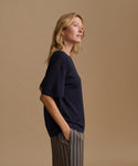 A model wearing a navy blue tee with stripe pants against a beige background.