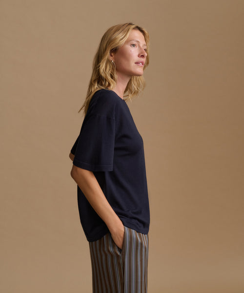 A model wearing a navy blue tee with stripe pants against a beige background.