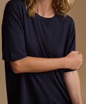 A close up image of a model wearing a navy blue tee with stripe pants against a beige background.
