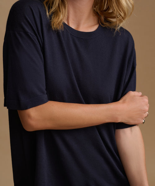 A close up image of a model wearing a navy blue tee with stripe pants against a beige background.