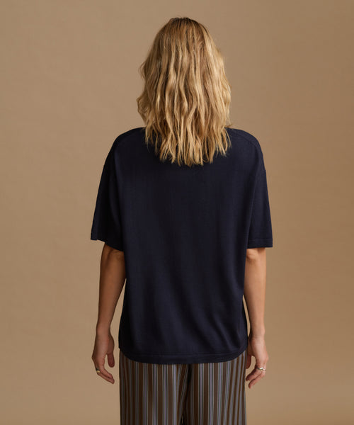 A model wearing a navy blue tee with stripe pants against a beige background.