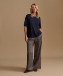 A model wearing a navy blue tee with stripe pants against a beige background.
