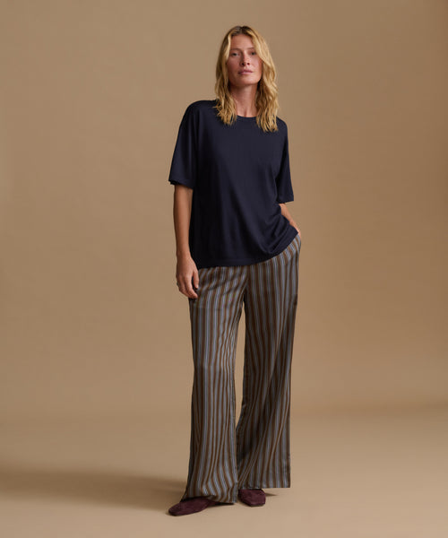 A model wearing a navy blue tee with stripe pants against a beige background.