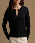 A woman wearing a black long-sleeve button-front cardigan with a relaxed fit, paired with light beige pants, set against a solid warm brown background.