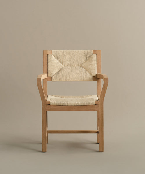 The Montecito Dining Arm Chair has a warm oak frame, clean lines, armrests, and a woven Danish paper cord seat and backrest for a simple modern look.