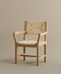 The Montecito Dining Arm Chair showcases a natural warm oak finish with beige Danish paper cord seat and backrest panels, all highlighted against a plain taupe background.