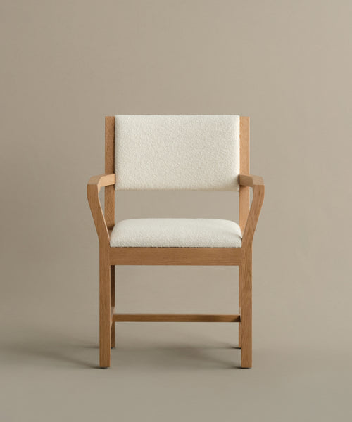 The Montecito Upholstered Dining Arm Chair features a wooden frame with clean lines, a minimalist design, and light beige upholstered seat and backrest, displayed against a plain taupe background.
