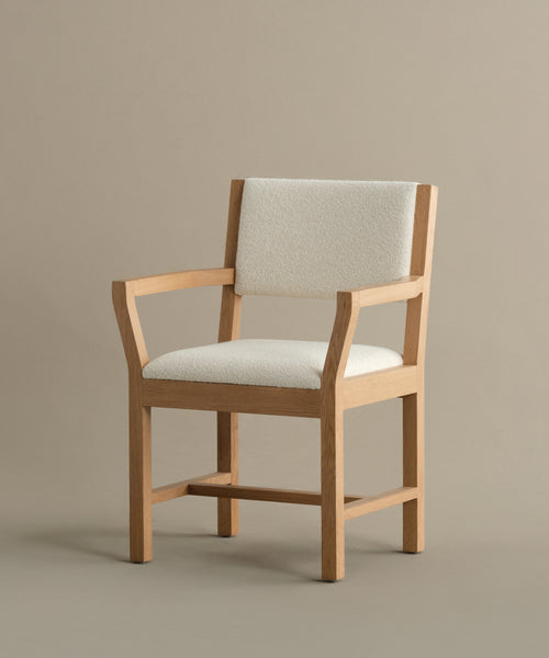 The Montecito Upholstered Dining Arm Chair features light beige fabric upholstery on the seat and backrest, wooden frame, clean lines, and a minimalist design, set against a plain neutral background.