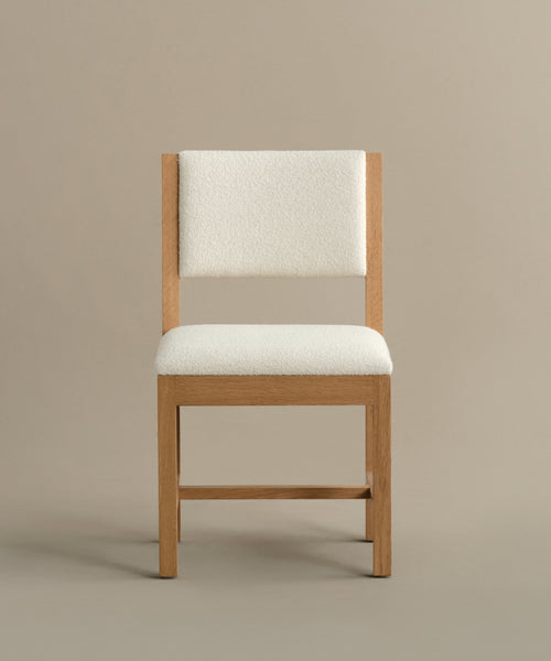 The Montecito Upholstered Dining Chair features a simple white oak frame and ivory boucle padded seat and backrest, shown against a plain beige background.
