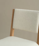 A close-up of the Montecito Upholstered Dining Chair, featuring a white oak frame and ivory boucle seat and backrest, set against a plain beige background.
