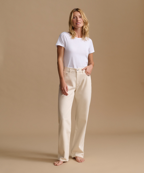 Model wearing cream color jeans with a cream t-shirt against a beige studio background.