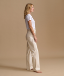 Model wearing cream color jeans with a cream t-shirt against a beige studio background.