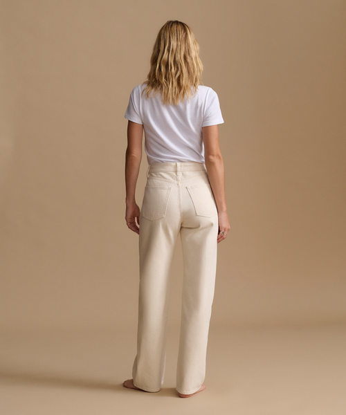 Model wearing cream color jeans with a cream t-shirt against a beige studio background.
