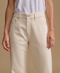 Model wearing cream color jeans with a cream t-shirt against a beige studio background.