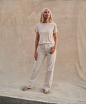 Model wearing cream color jeans with a cream t-shirt at the beach.