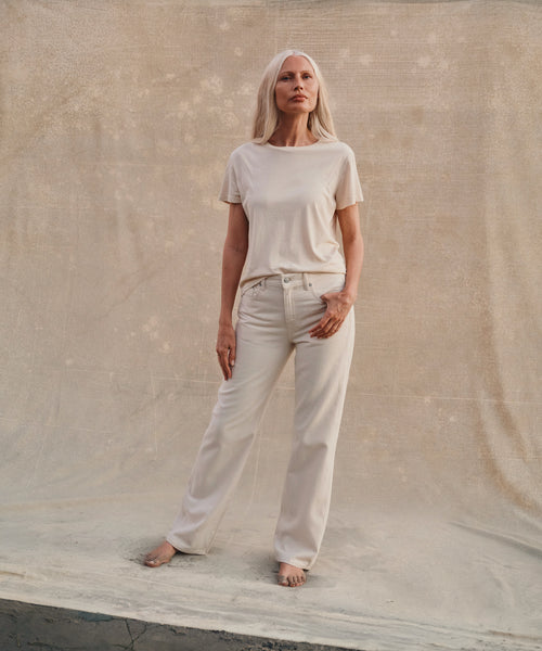 Model wearing cream color jeans with a cream t-shirt at the beach.