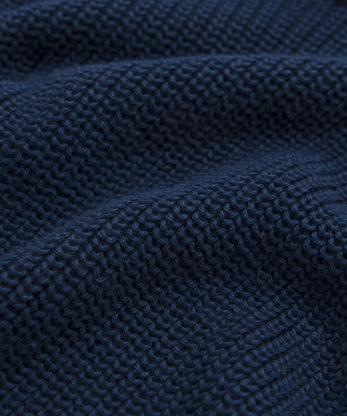 Close-up of dark blue textured fabric from the Oversized Cotton Fisherman, showcasing a waffle-knit pattern with small raised squares and soft, wavy folds—ideal for cozy womens knitwear.