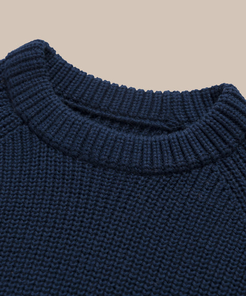 Close-up of the Oversized Cotton Fisherman sweater in navy blue, featuring a ribbed crew neckline and detailed texture, displayed against a plain beige background.