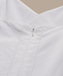 Close-up of the Peninsula Dress in Italian washed poplin, showing its V-neck back, small silver zipper, vertical stitching, and smooth white fabric against a beige background.