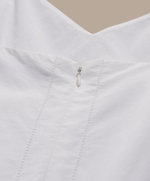 Close-up of the Peninsula Dress in Italian washed poplin, showing its V-neck back, small silver zipper, vertical stitching, and smooth white fabric against a beige background.