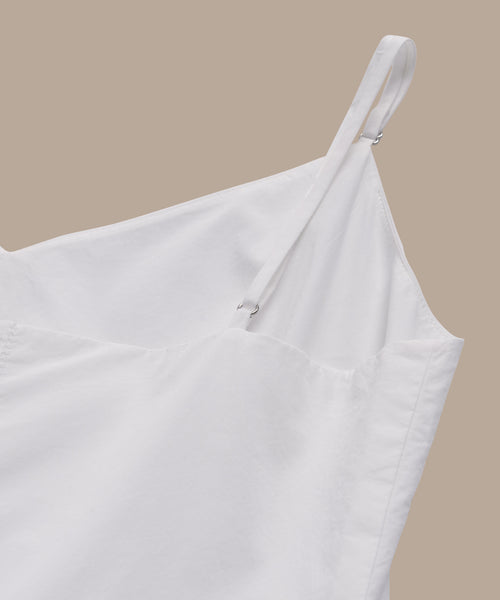 Close-up of the Peninsula Dress, a white dress featuring thin, adjustable straps against a plain beige background. Its lightweight fabric resembles Italian washed poplin, providing a smooth and airy feel.
