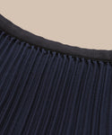 Close-up of the Pleated Skirt in navy with a black waistband, displayed against a beige background.