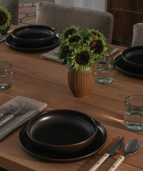 A vase with sunflowers on a dining table set with dinnerware. 