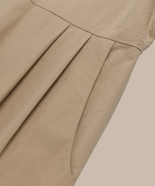 Close-up of the Rove Dress in beige cotton, featuring neatly sewn pleats and a pocket detail. The smooth fabric is shown against a matching beige background for a stylish monochromatic look.