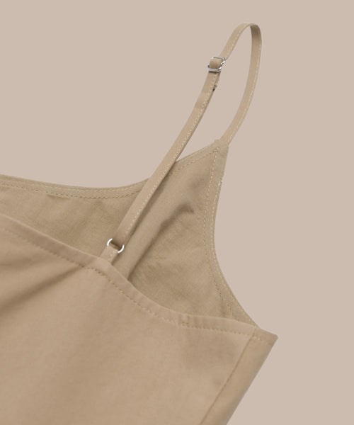 Close-up of the Rove Dress in khaki, featuring spaghetti straps and adjustable ties. Set against a beige background, its smooth matte fabric makes it the perfect choice for spring.