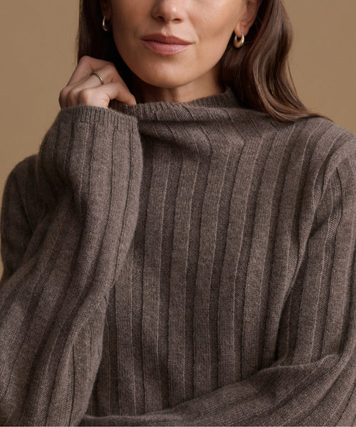 Close-up of a woman wearing a ribbed knit sweater in a warm taupe-brown color, with a soft beige background.