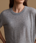 Close-up of a person wearing a heather gray short-sleeve crewneck knit top against a warm tan background.