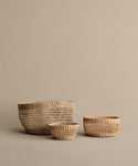 Three Seagrass Produce Bowls in different sizes are displayed on a beige background, perfect for kitchen storage or as fruit bowls, with the largest bowl at the back and two smaller ones in front.