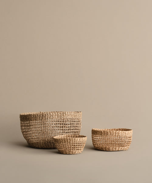 Three Seagrass Produce Bowls in different sizes are displayed on a beige background, perfect for kitchen storage or as fruit bowls, with the largest bowl at the back and two smaller ones in front.