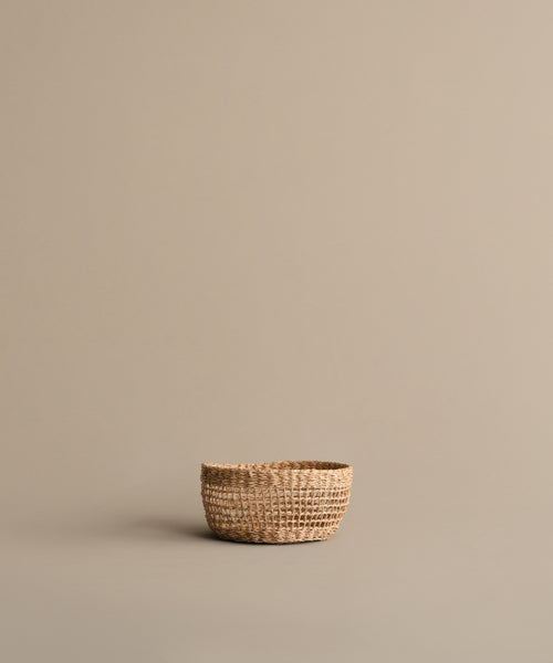 The Seagrass Produce Bowl is a small, empty bowl on a light brown surface with a beige background, ideal for kitchen storage or displaying fresh fruit.