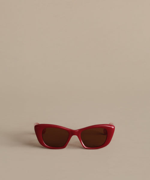 Sierra Sunglasses, featuring a red retro cat eye frame and dark lenses with 100% UV protection, are displayed on a plain beige background.
