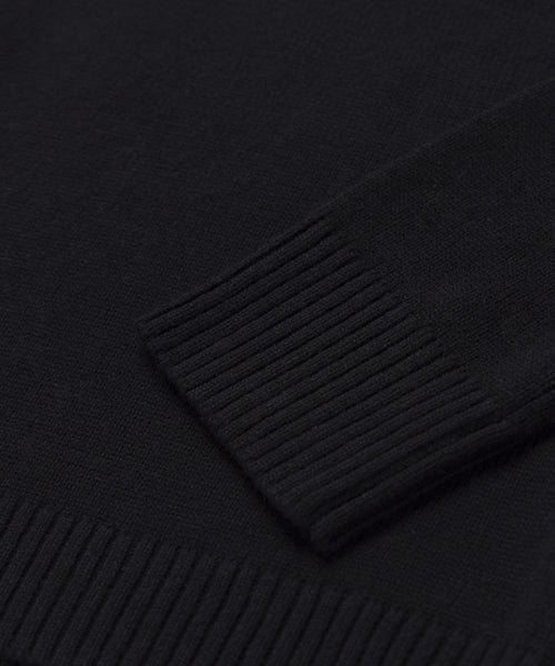 A close-up of the Simone V-Neck sweater in black highlights its ribbed sleeve cuff and hem, showcasing the fine, even knit pattern in soft cotton merino—an ideal everyday layer.