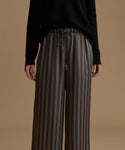 A model wearing high-waisted, wide-leg trousers with vertical brown, beige, and gray stripes, paired with a black long-sleeve top.