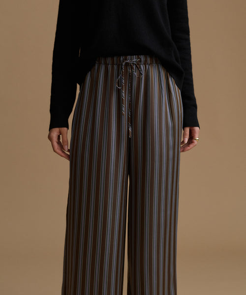A model wearing high-waisted, wide-leg trousers with vertical brown, beige, and gray stripes, paired with a black long-sleeve top.