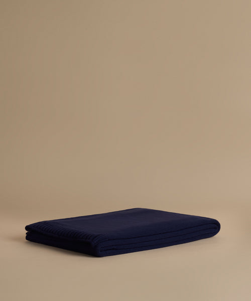 A folded navy blue ribbed knit blanket or throw is displayed on a warm beige studio background.