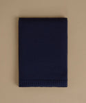 A folded navy blue knit blanket with a ribbed border, displayed flat against a solid beige background.