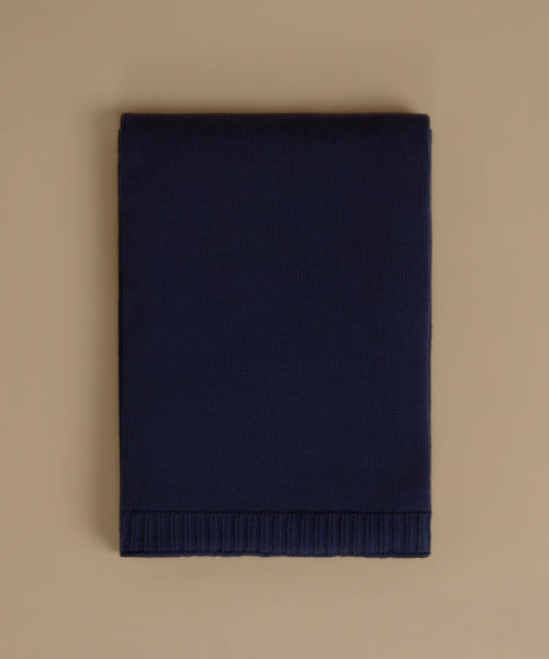 A folded navy blue knit blanket with a ribbed border, displayed flat against a solid beige background.