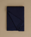 A folded navy blue knit blanket with ribbed borders, displayed on a solid beige background.