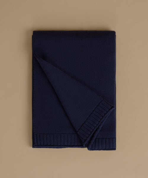 A folded navy blue knit blanket with ribbed borders, displayed on a solid beige background.