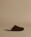 A single brown suede mule clog with a cream sherpa lining, shown in profile against a solid beige background.