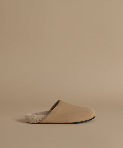 A single beige slip-on mule clog with a soft textured lining, shown in profile against a solid beige background.